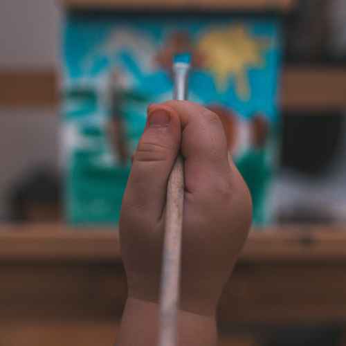 Eine Kinderhat mit einem Pinsel vor einer unscharfen Leinwand