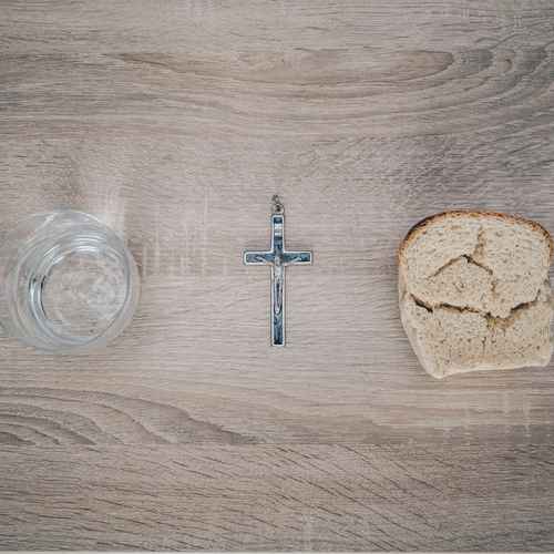 ein Glas mit Wasser, Brot und ein Kreuz auf einem Holztisch